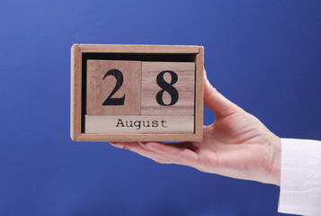 Female Hand holding wooden block calendar with the date August 28 on a blue background