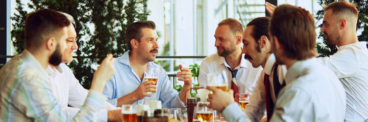 Cheerful people, businessmen, colleagues sitting at outdoor bar, restaurant, drinking beer, talking, discussing successful projects and partnership. Concept of business, meeting, fun, Oktoberfest