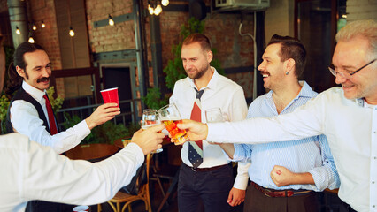 Relaxing meeting, businessmen in formal wear gathering at outdoor bar, drinking beer, talking, laughing after hard working week. Concept of business, meeting, fun, leisure time, Oktoberfest