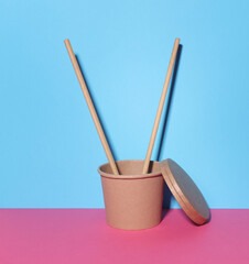 Cardboard eco container with Chinese chopsticks on blue pink background