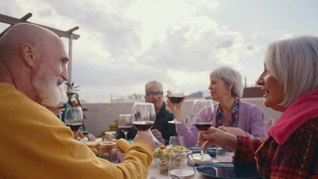 Cinematic footage of a group of seniors eating on a rooftop terrace of a beautiful house. Old friends reunited, having fun remembering stories and sharing good food. Concept about seniority.
