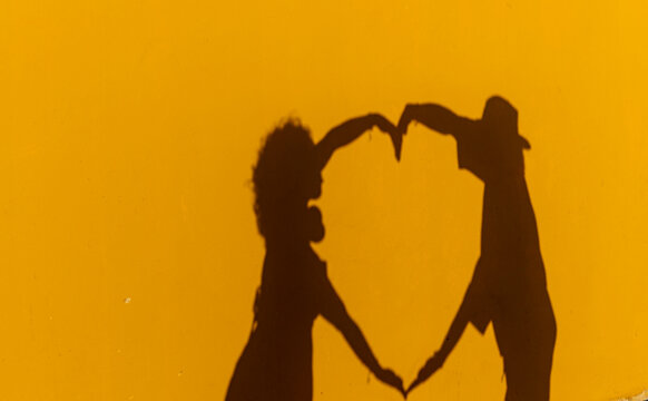 Couple forms heart shape with hands against yellow background