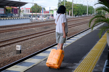 A woman pulling an orange luggage on a train station platform