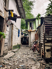 Metro Manila, Philippines - Aug 28, 2024: A narrow, cluttered alley in a local slum, lined with makeshift homes and scattered debris.