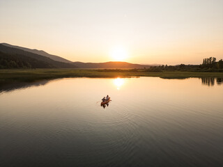 Couple canoeing at sunset, two silhouettes paddling a canoe on a beautiful lake in the evening, aerial shot. Nature enjoyment and relaxation concepts.