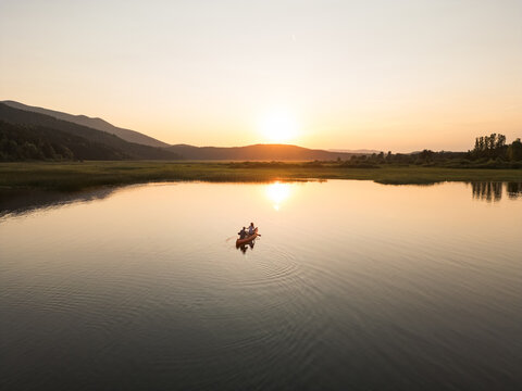 Couple canoeing at sunset, two silhouettes paddling a canoe on a beautiful lake in the evening, aerial shot. Nature enjoyment and relaxation concepts.