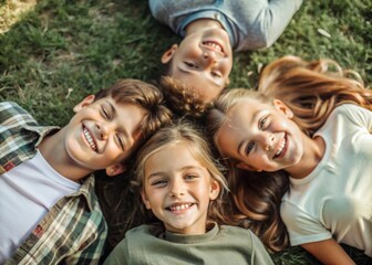 Obraz premium Happy children, two boys and two girls lie on the grass and look at the camera in the park on a summer day.Top view.