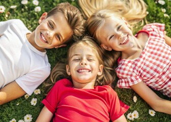 Happy children, a boy and two girls lie on the grass and look at the camera in the park on a summer day.Top view.