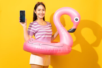 Smiling Asian woman with a mobile phone and a rubber ring, wearing t-shirts featuring coconut tree flowers, vibrant yellow backdrop, summer, © anon