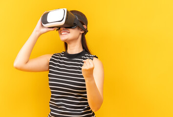 Fototapeta premium Asian young woman playing video games using mobile with headphones on yellow background isolated.