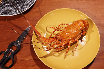 Freshly Cooked Lobster Served on a Yellow Plate with Scissors on the Side on a Table