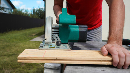 Carpenter sawing wood with handsaw. Male carpenter using electric circular saw. Wood chips flying....