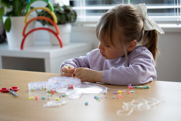 A sweet girl enthusiastically makes a bracelet of beads. A creative child engaged in jewelry making