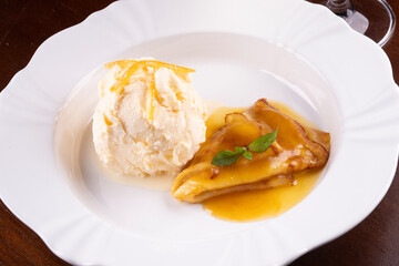 crepe suzette dessert with scoop of vanilla ice cream and orange slices up close