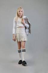 A girl in a white crop top and plaid skirt stands holding a matching jacket, embodying a playful yet stylish look. The scene emphasizes modern, casual fashion for young girls.