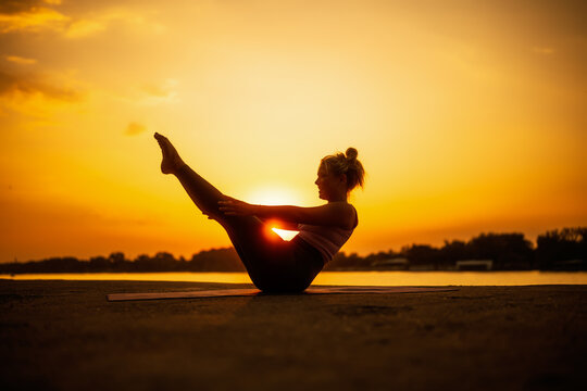 Woman exercising pilates in sunset. Teaser exercise.