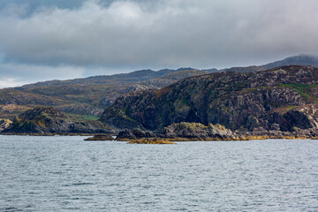 Naklejka premium View of Scottish mainland from a ship, Image shows beautiful landscape coastal views of the mainland from a ship following the coastline image shows calm seas with heavy cloud and hilly terrain