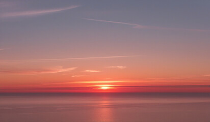 Fototapeta premium a sunset is visible over the ocean and the sky is orange and blue.