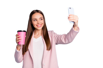 Portrait of cute cheerful lady using her cellphone making selfie holding mug with hot beverage wearing pink coat isolated over blue color background