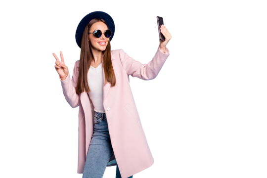 Portrait of cute content blog girl in eyewear eyeglasses making v-sign taking selfie having fun wearing pink stylish vercoat topcoat denim jeans isolated over blue background