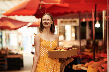 Box with peaches and grapes. Young woman is on the vegetable market or bazaar