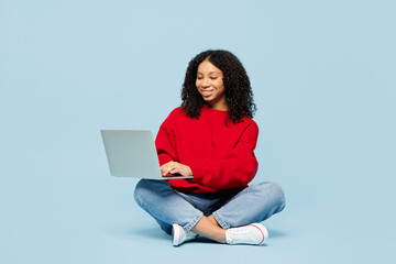 Full body little kid teen IT girl of African American ethnicity wear red sweatshirt sits hold use...