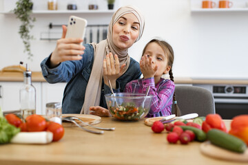 Mother and daughter in the kitchen enjoying time together, sharing moments, and promoting healthy eating habits. Muslim mother and daughter have a video call showing a healthy salad.