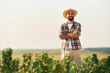 With arms crossed. Farmer is on the agricultural field