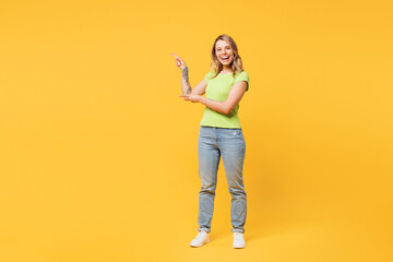 Full body young happy cheerful blonde woman she wear green t-shirt casual clothes point index finger aside on area mock up isolated on plain yellow orange background studio portrait Lifestyle concept