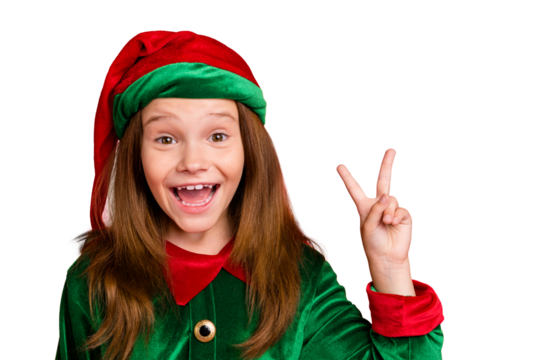 Close up photo of cheerful festive elf kid with long red head haircut in green hat wearing elf costume making v-signs isolated over red background
