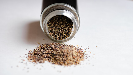 Grounded Black pepper spilling out of a pepper shaker on a white background