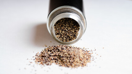 Grounded Black pepper spilling out of a pepper shaker on a white background