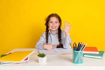 Portrait of little schoolchild girl desktop raise arm wave wear uniform isolated on yellow color background