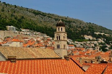 Obraz premium Dubrovnik's historic charm, with its iconic terracotta rooftops and church bell tower set against lush hills. A UNESCO World Heritage site, the Old Town blends history, culture, and natural beauty.
