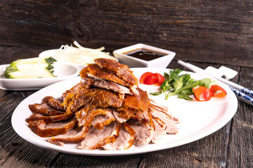 Peking Duck on a white plate served with fresh cucumber, green onions, cilantro and roasted wheaten chinese pancakes on black  wooden background. Chinese food. food concept.