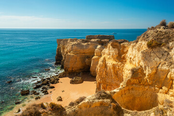 Yellow cliff rock formations over secret sandy beach near Albufeira, Algarve region, Portugal, Europe. Popular touristic destination for summer vacation on Portuguese Atlantic coast