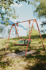 old Soviet metal colored swing for children on the street against the background of trees and church