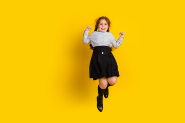 Full body portrait of little schoolkid girl jump raise fists wear uniform isolated on yellow color...