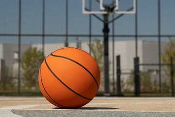 Basketball orange ball lies at outdoor public basketball court. Sports gear without people. Template, sport background. Close up.