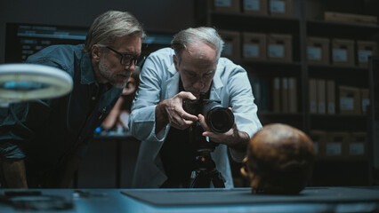 Two archaeologists talk and take photo of fossil remains of prehistoric human skull using...