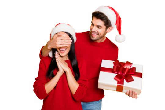 Portrait of handsome man with brown hair hide his excited wife eyes give her package wear red pullover isolated over yellow background