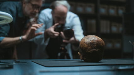 Two archaeologists talk and take photo of fossil remains of prehistoric human skull using...