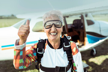 Smiling senior woman giving thumbs up before skydiving