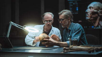 Two archaeologists take measurements of ancient human skull, study fossil remains, use tablet...