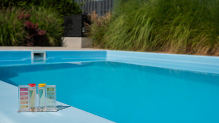 A pool water testing kit displaying pH and chlorine levels is set on the pool's edge, with a blurred green background highlighting the importance of water quality.