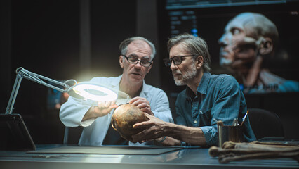 Two archaeologists take measurements of ancient human skull, study fossil remains, use tablet...