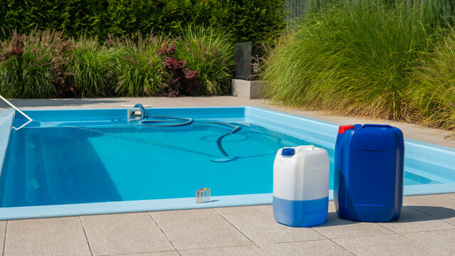 A poolside scene with large chemical containers, a cleaning hose in the pool, and a water testing kit, highlighting pool maintenance essentials.