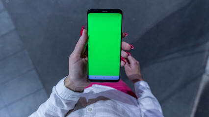 Female teen girl with red nails using smartphone with green screen staying outdoors.