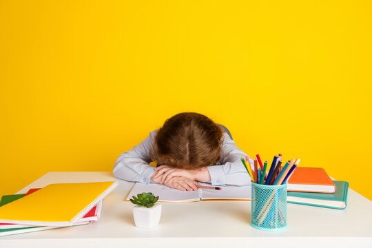 Portrait of little schoolchild girl fell asleep desk wear uniform isolated on yellow color background