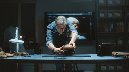Mature archaeologist takes photo of fossil remains of prehistoric human skull in archaeological...